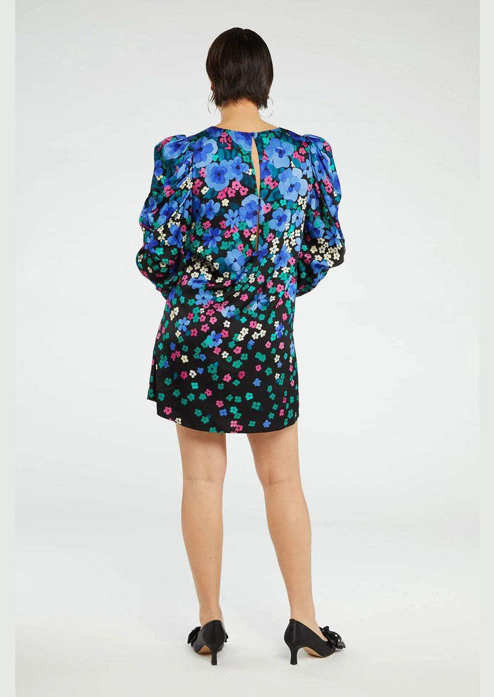 Woman wearing short floral dress with puff sleeves in blue, purple, and green, back view