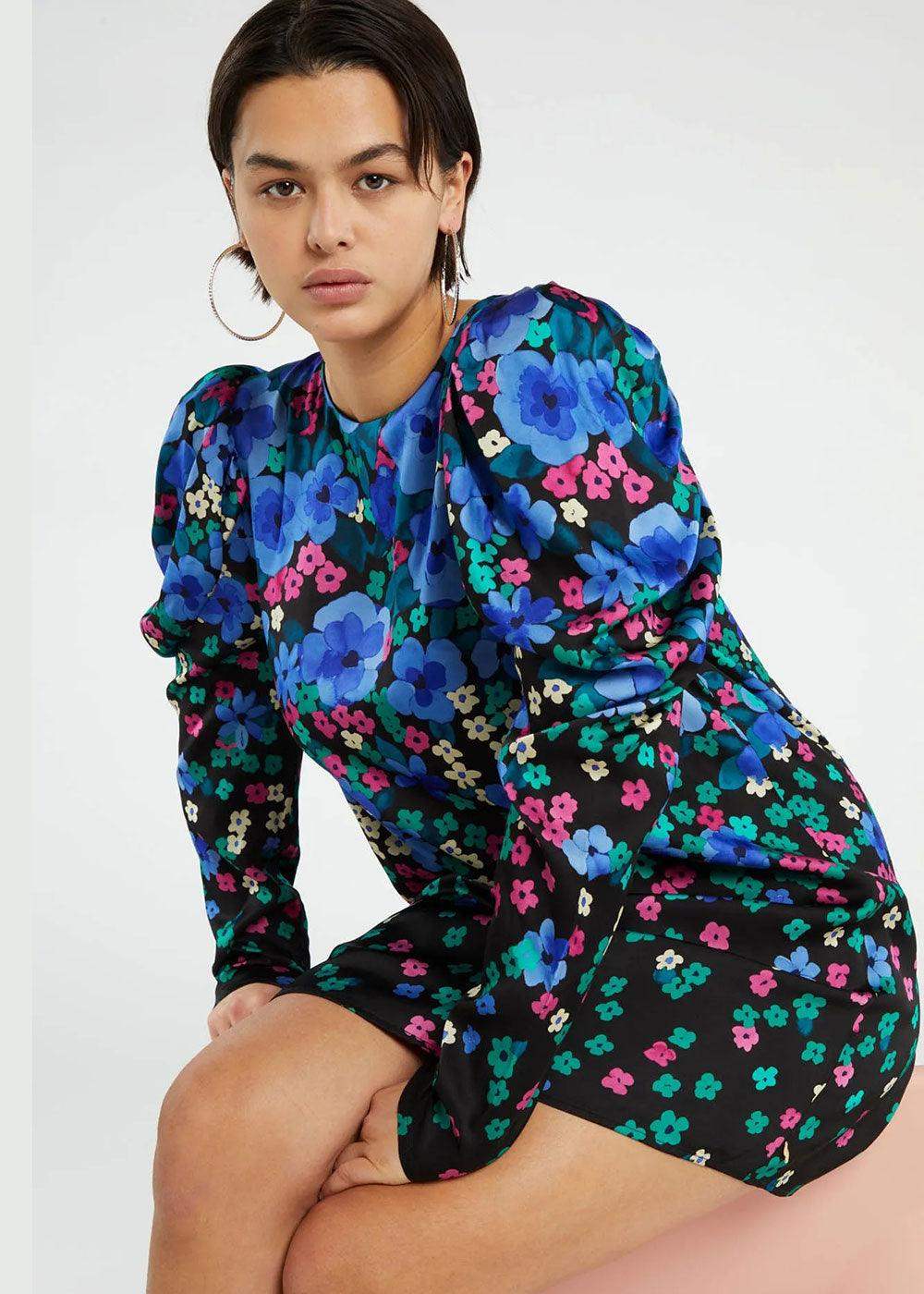 Woman wearing a long-sleeve mini dress with bold blue and pink floral print on black.