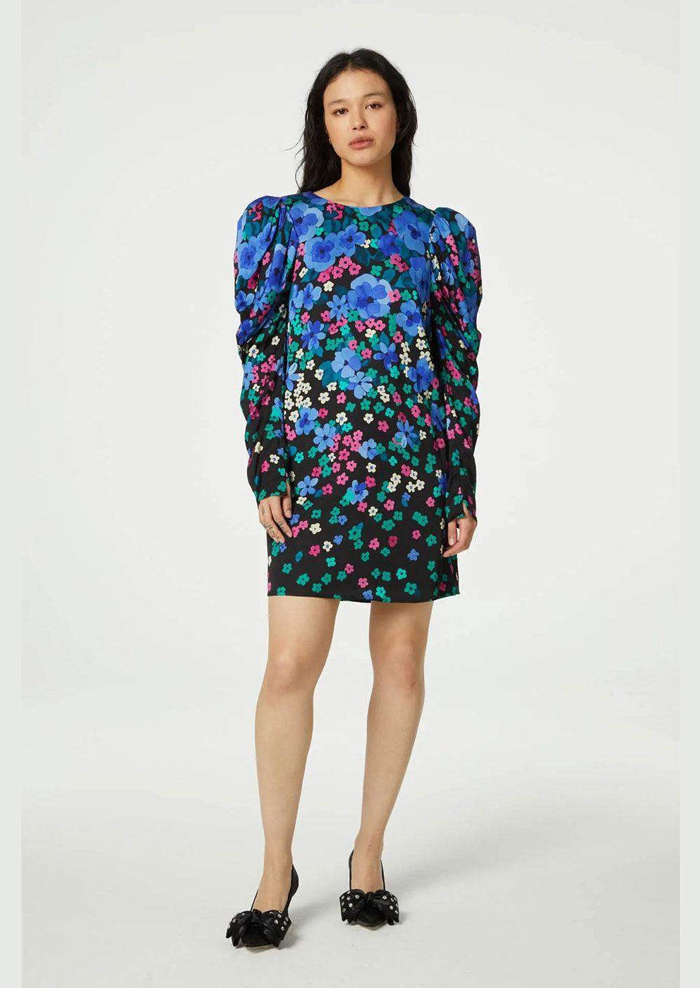 Woman wearing a bright floral mini dress with puffed sleeves against a plain background