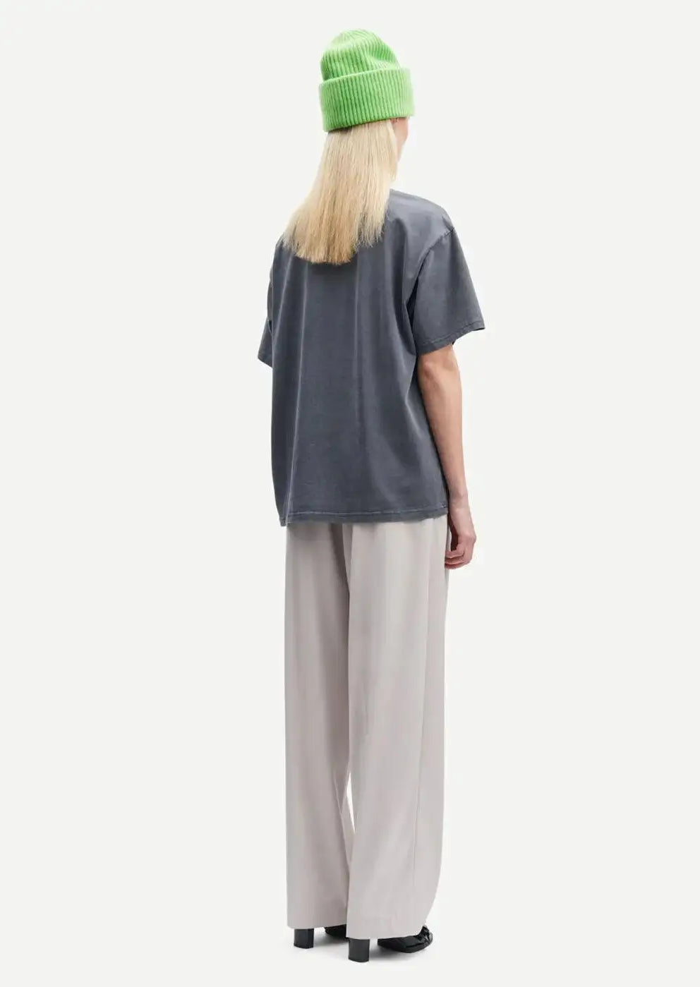 Woman wearing light grey wide-leg trousers, dark t-shirt, and green beanie, rear view