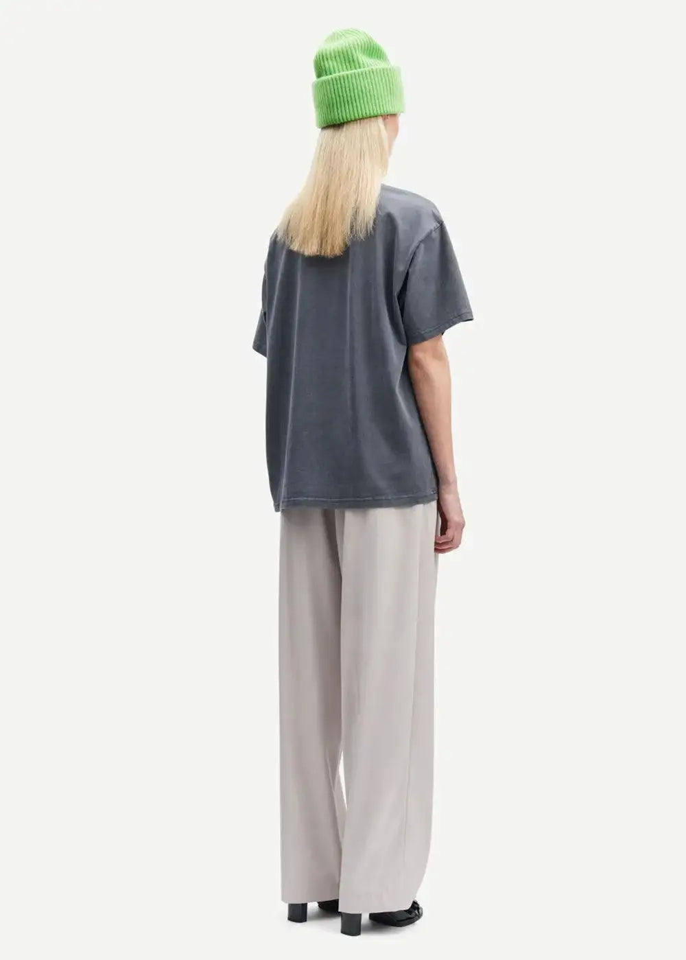 Woman wearing light grey wide-leg trousers, dark t-shirt, and green beanie, rear view