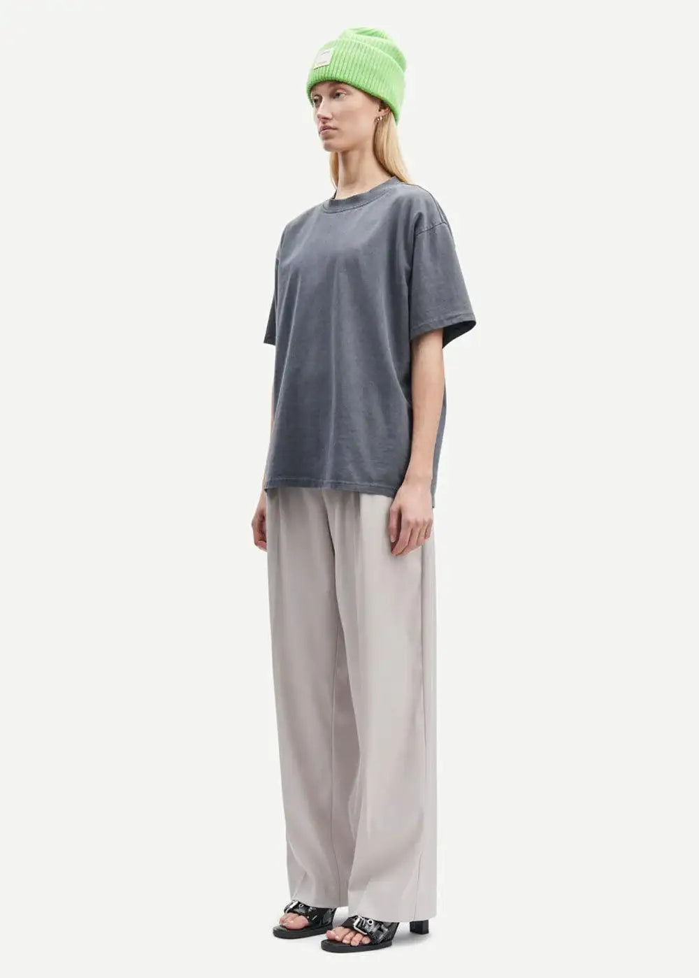 Woman in loose grey t-shirt, light beige wide-leg trousers, green beanie, and heeled sandals