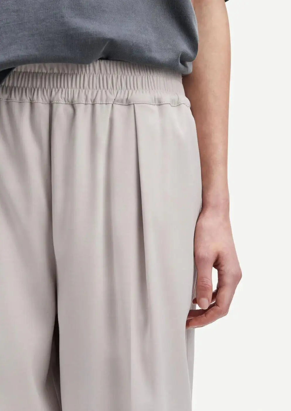 Light beige pleated trousers with elastic waistband, relaxed fit, close-up view