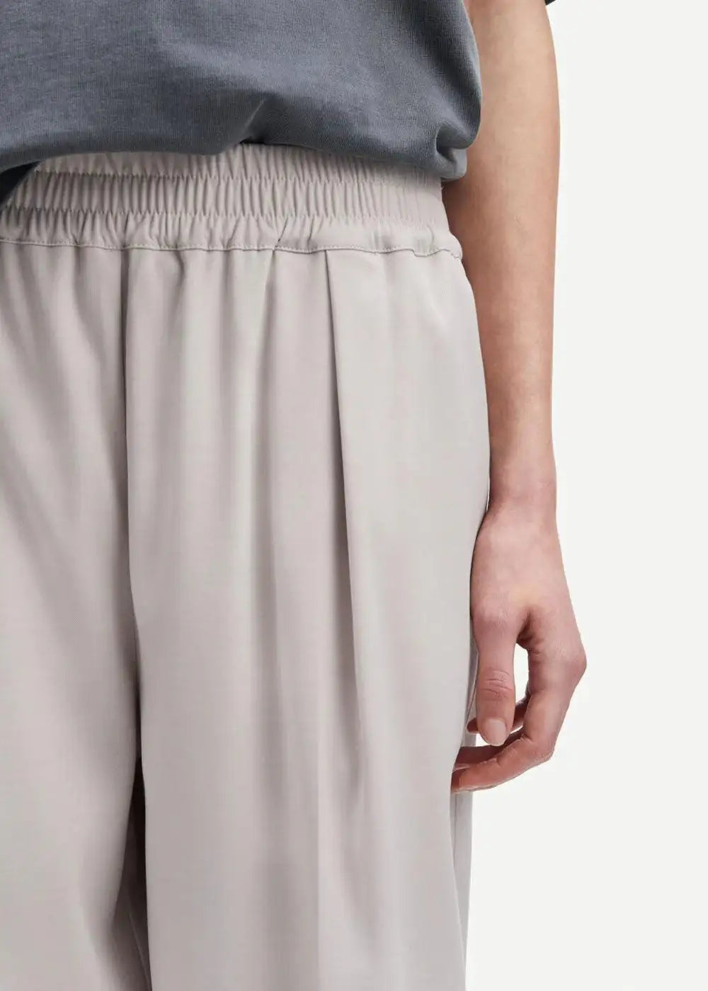 Light beige pleated trousers with elastic waistband, relaxed fit, close-up view