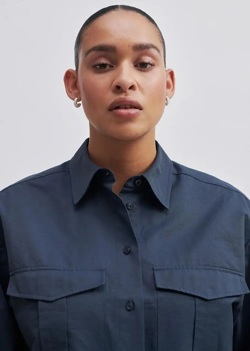 Woman wearing navy button-up shirt with chest pockets, minimal backdrop, close-up view