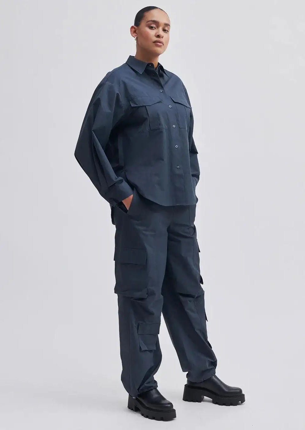 Woman wearing dark blue cargo trousers and matching oversized shirt with chunky black boots.
