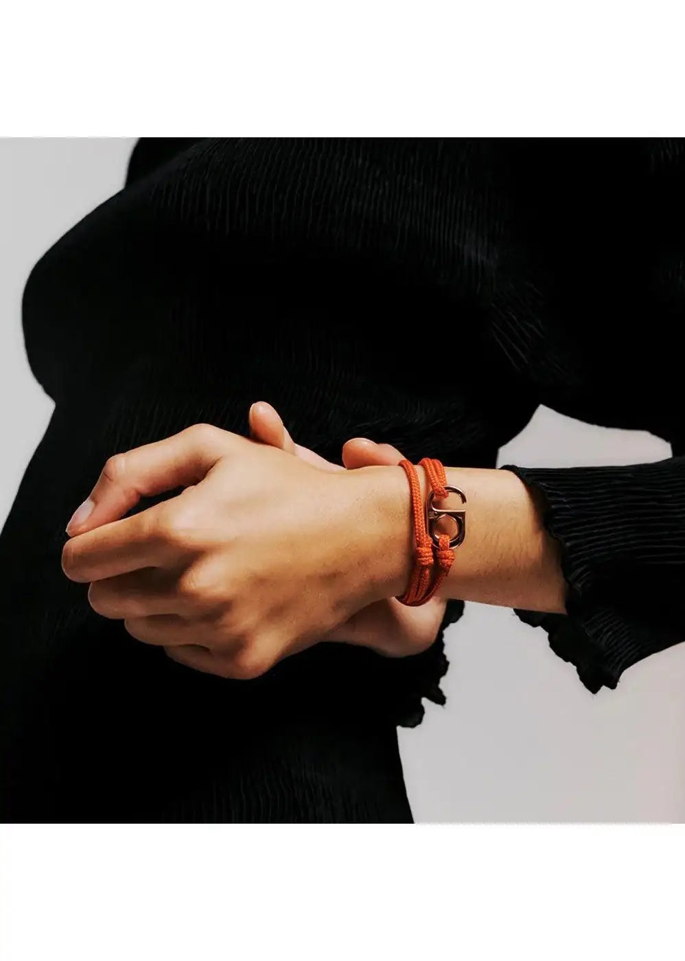 Orange rope bracelet with metal clasp on wrist, worn with long sleeve black top