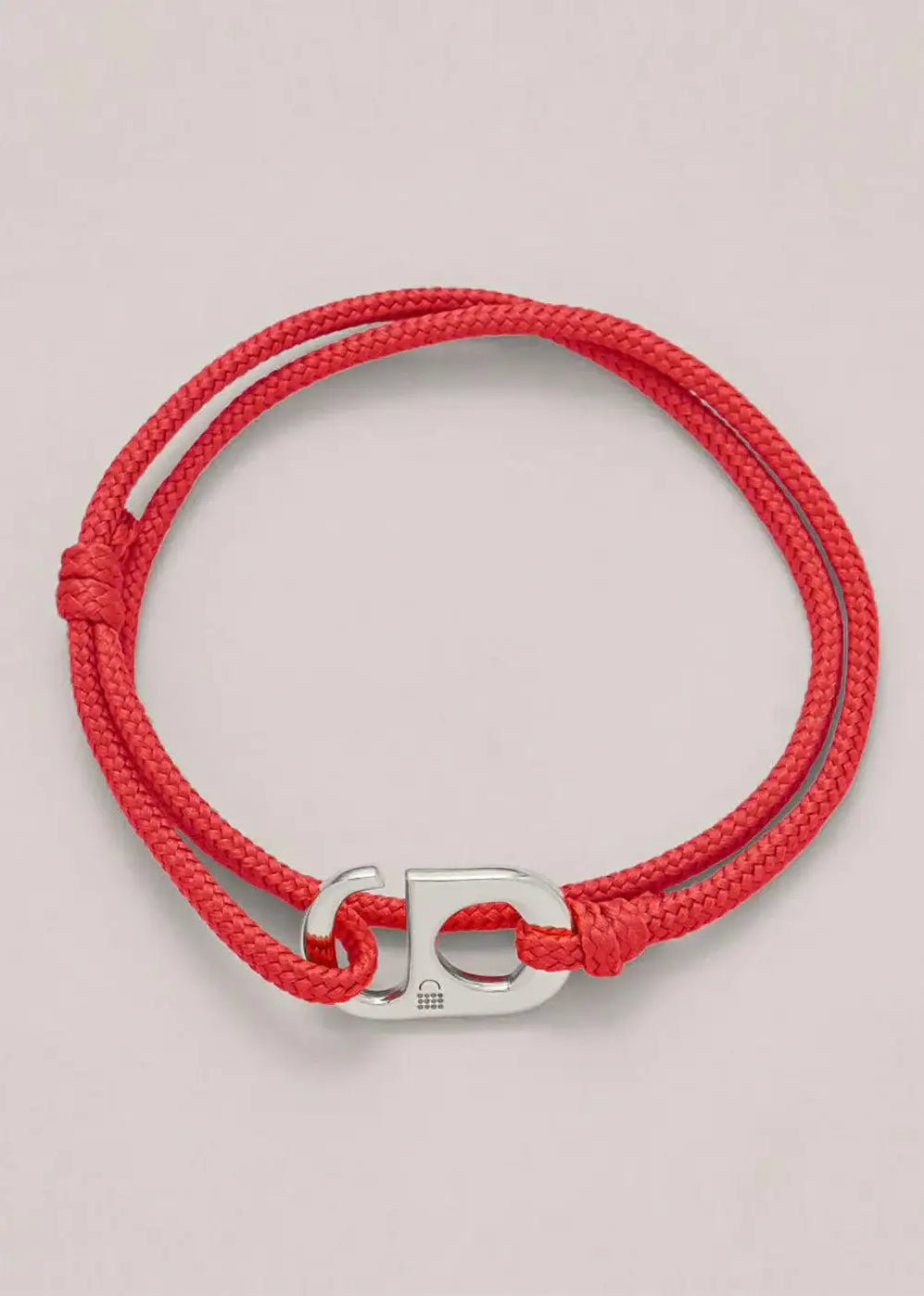 Red cord bracelet with a silver clasp on a neutral background, minimalist jewelry accessory.