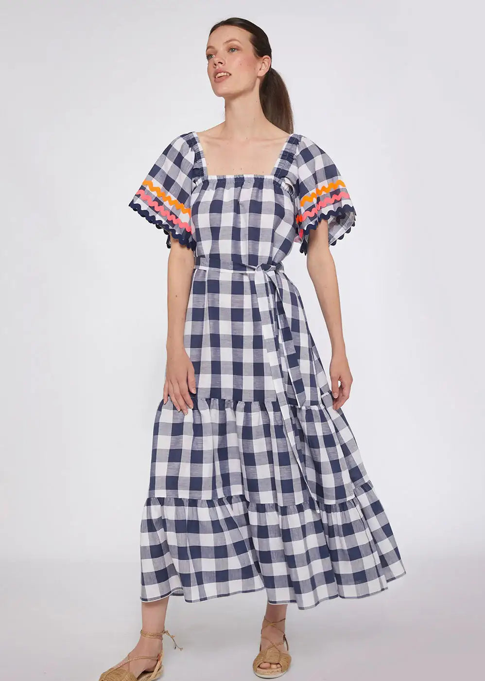 Woman wearing navy gingham tiered midi dress with flared sleeves and colorful trim.