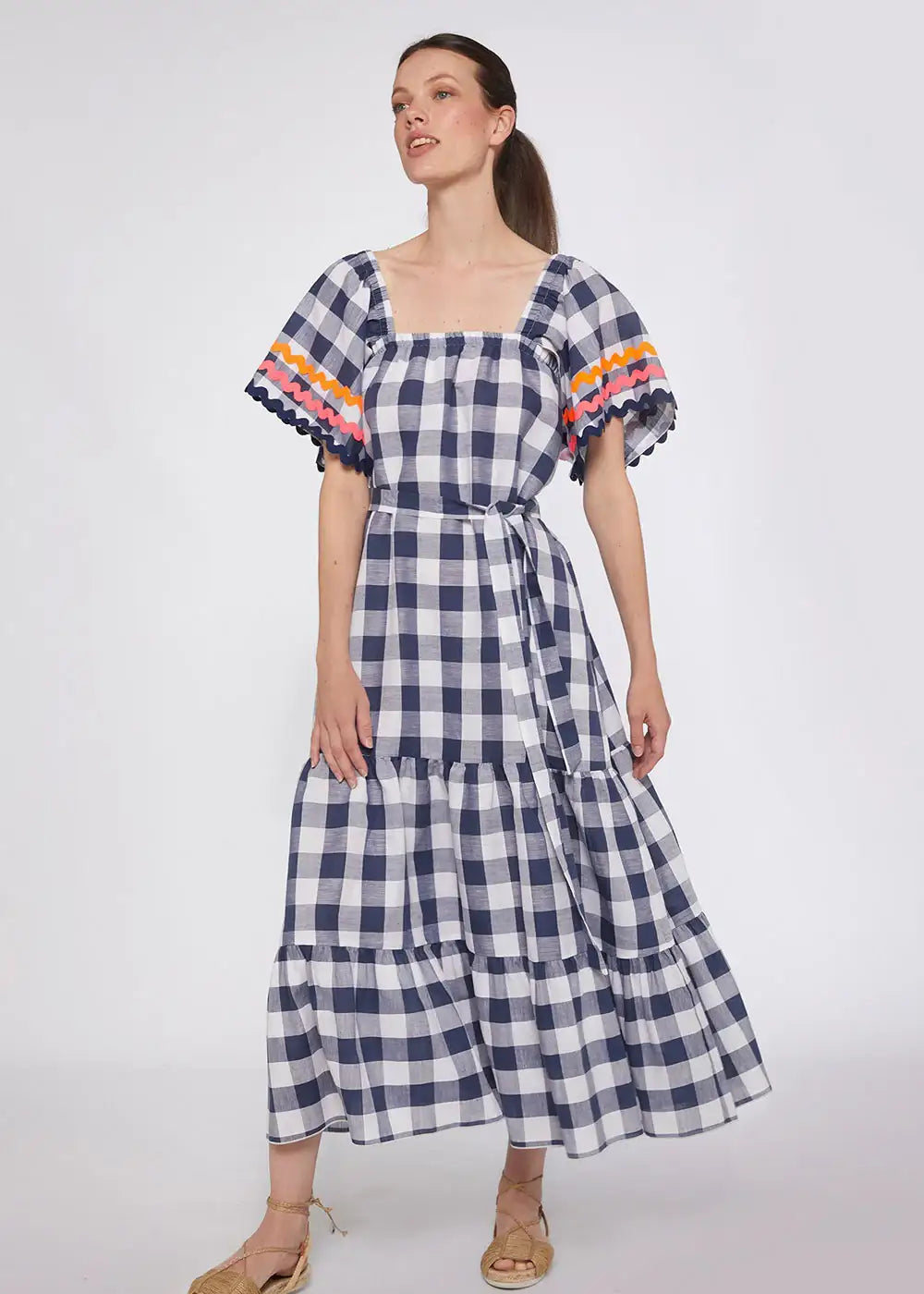 Woman wearing navy gingham tiered midi dress with flared sleeves and colorful trim.