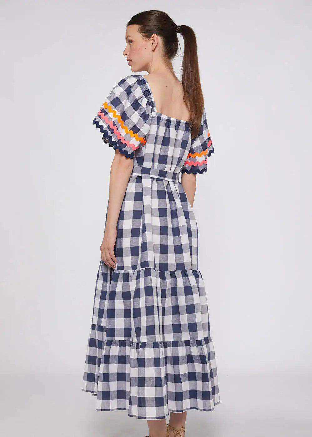 Woman wearing navy gingham checked midi dress with colorful ruffled sleeves, back view