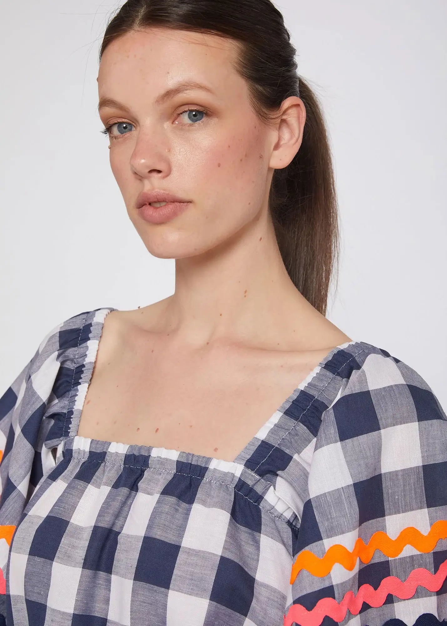 Woman wearing navy and white checkered dress with square neckline and colorful trim sleeves