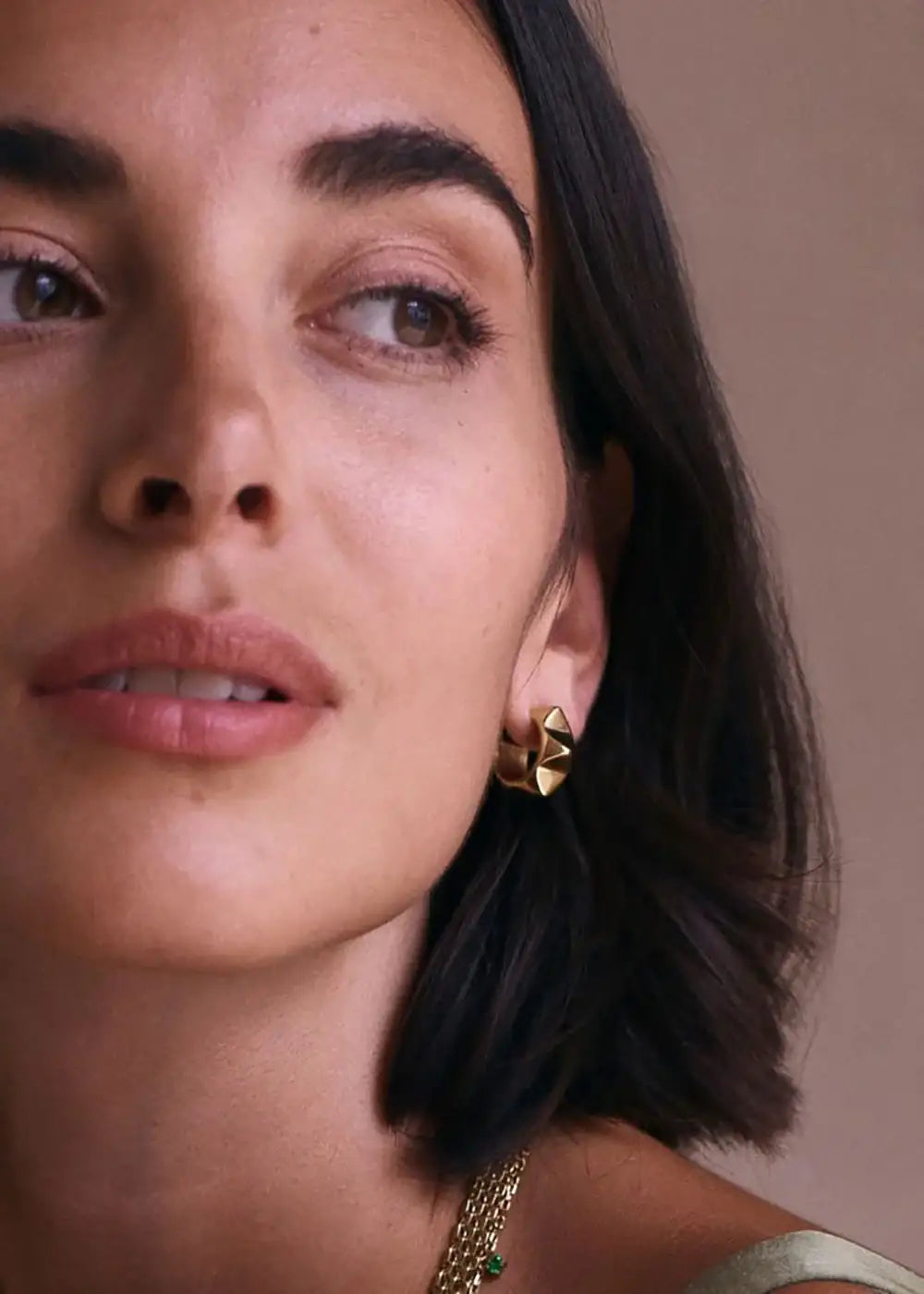 Woman wearing geometric gold hoop earrings and layered gold necklace, close up
