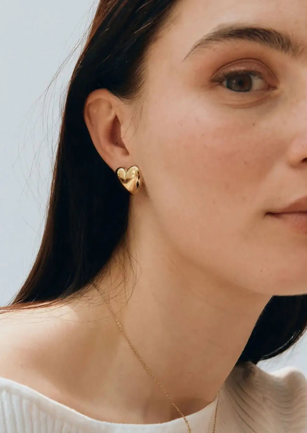 Gold heart-shaped stud earring worn by woman with long dark hair