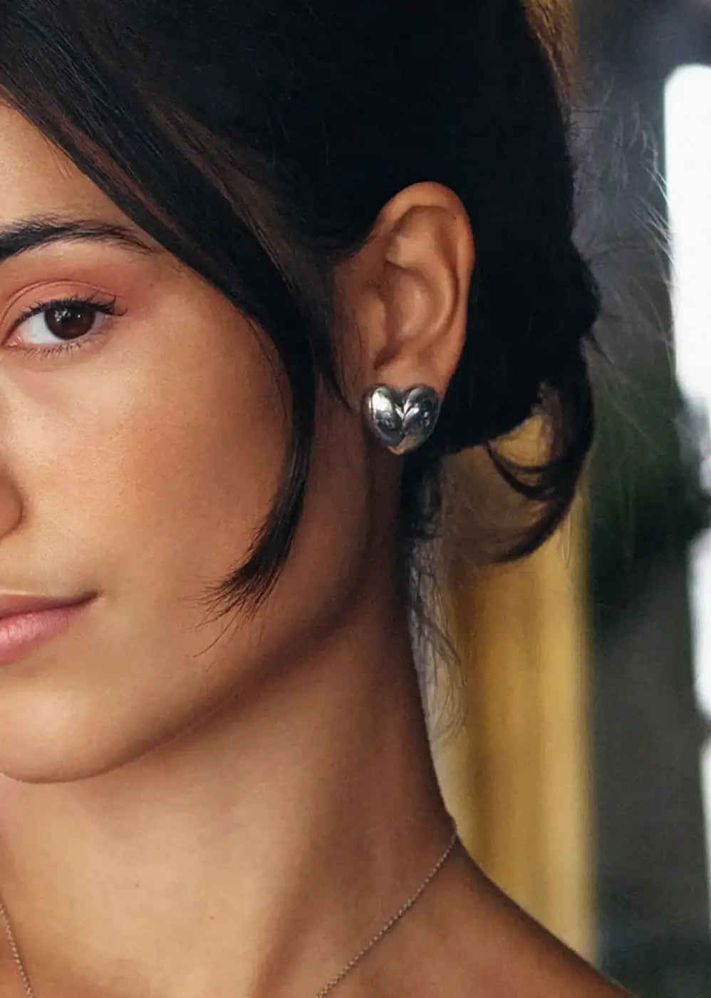 Woman wearing heart-shaped silver stud earrings, close-up of ear and jewelry