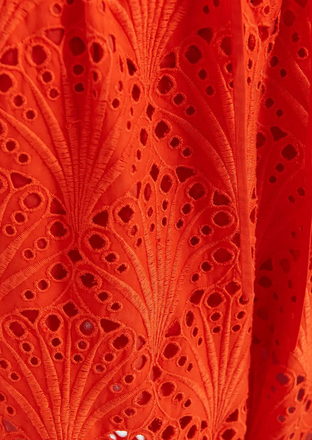 Close-up of vibrant orange embroidered lace fabric with intricate cut-out patterns