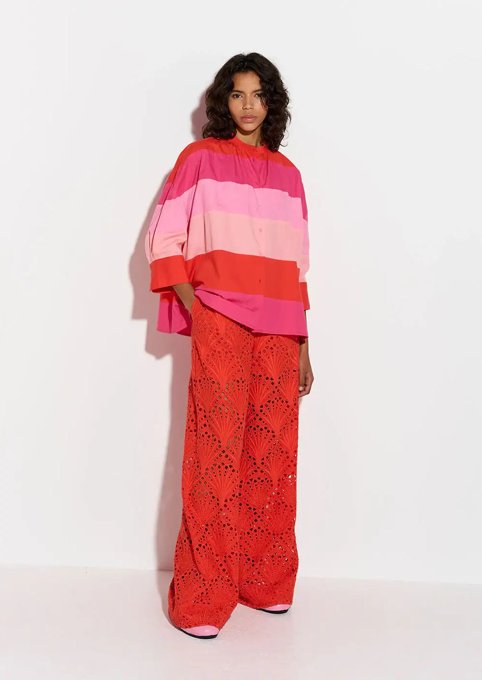 Woman in a pink and red striped oversized shirt and red lace wide-leg trousers