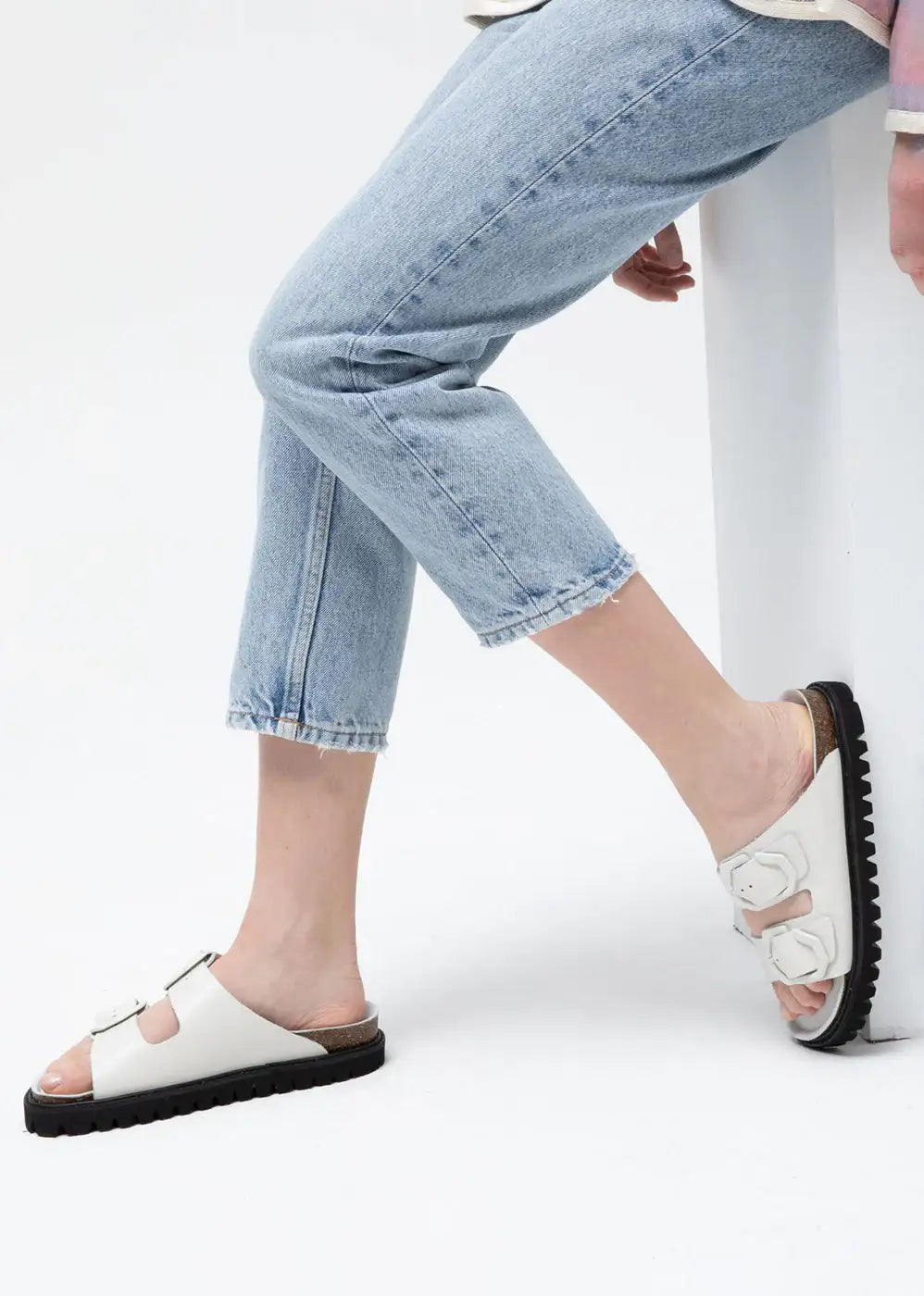 Woman wearing light blue cropped jeans and white double-strap sandals with black soles