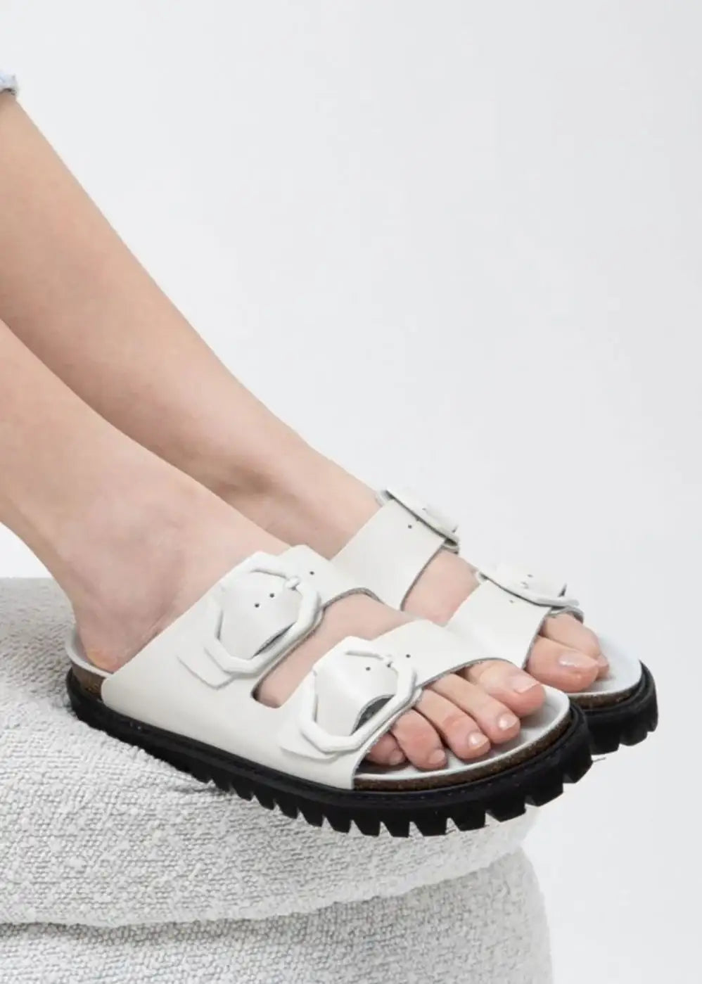 White double strap slide sandals with chunky black sole and geometric buckles on feet