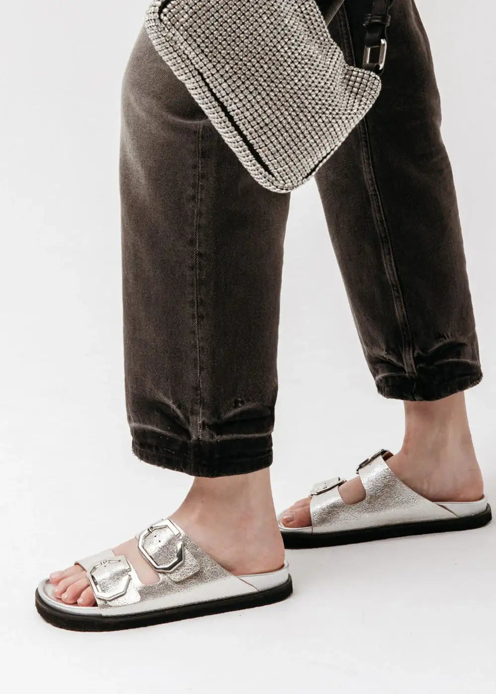 Woman wearing silver buckle sandals, black jeans, and a silver mesh purse