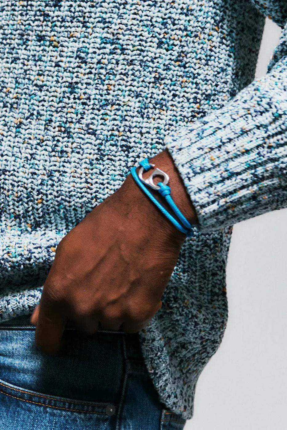 Man wearing blue rope bracelet with silver charm, styled with blue knit sweater and denim jeans