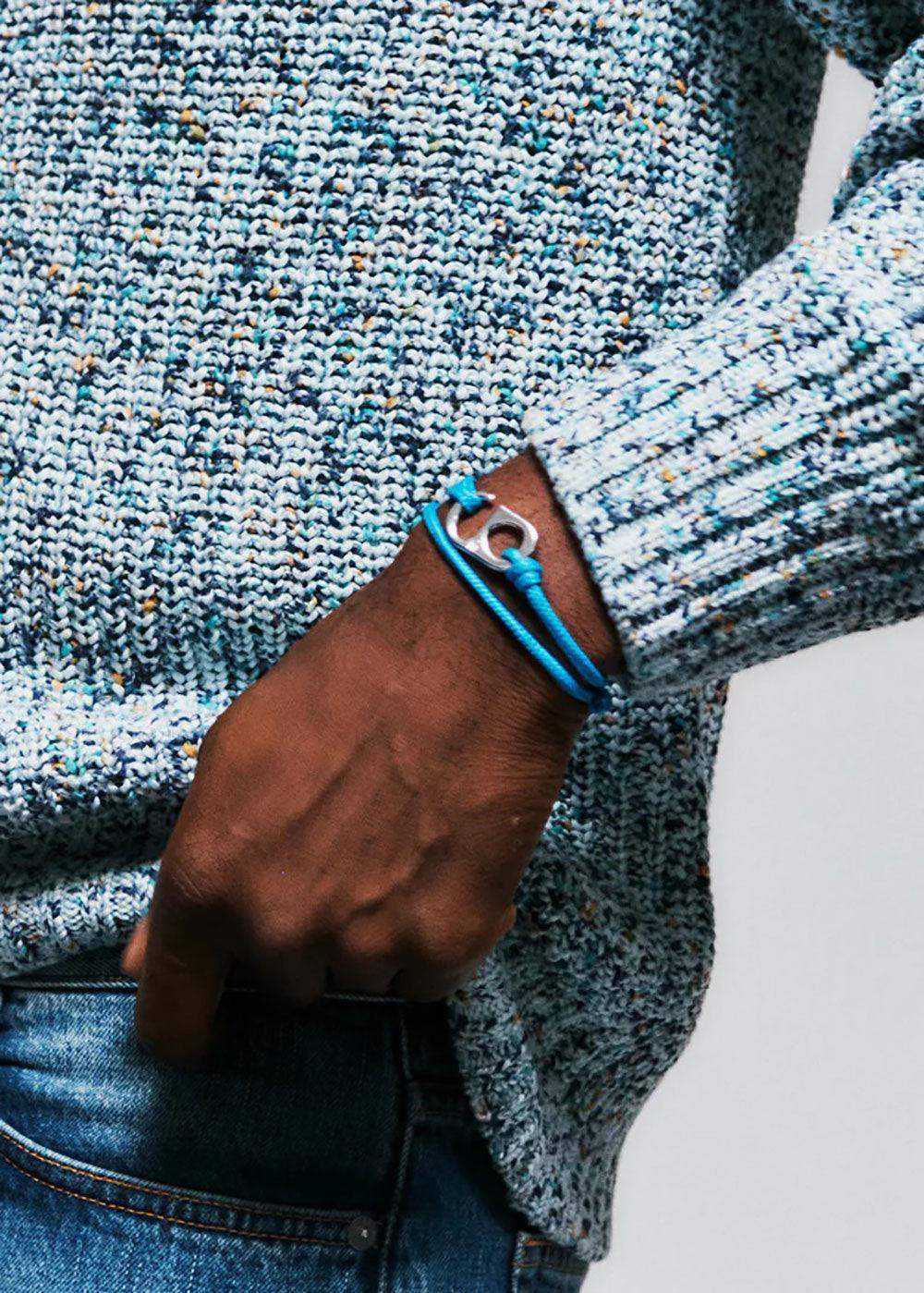 Man wearing blue rope bracelet with silver charm, styled with blue knit sweater and denim jeans