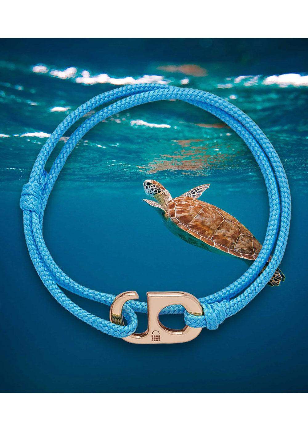 Blue braided bracelet with gold clasp, sea turtle swimming underwater background