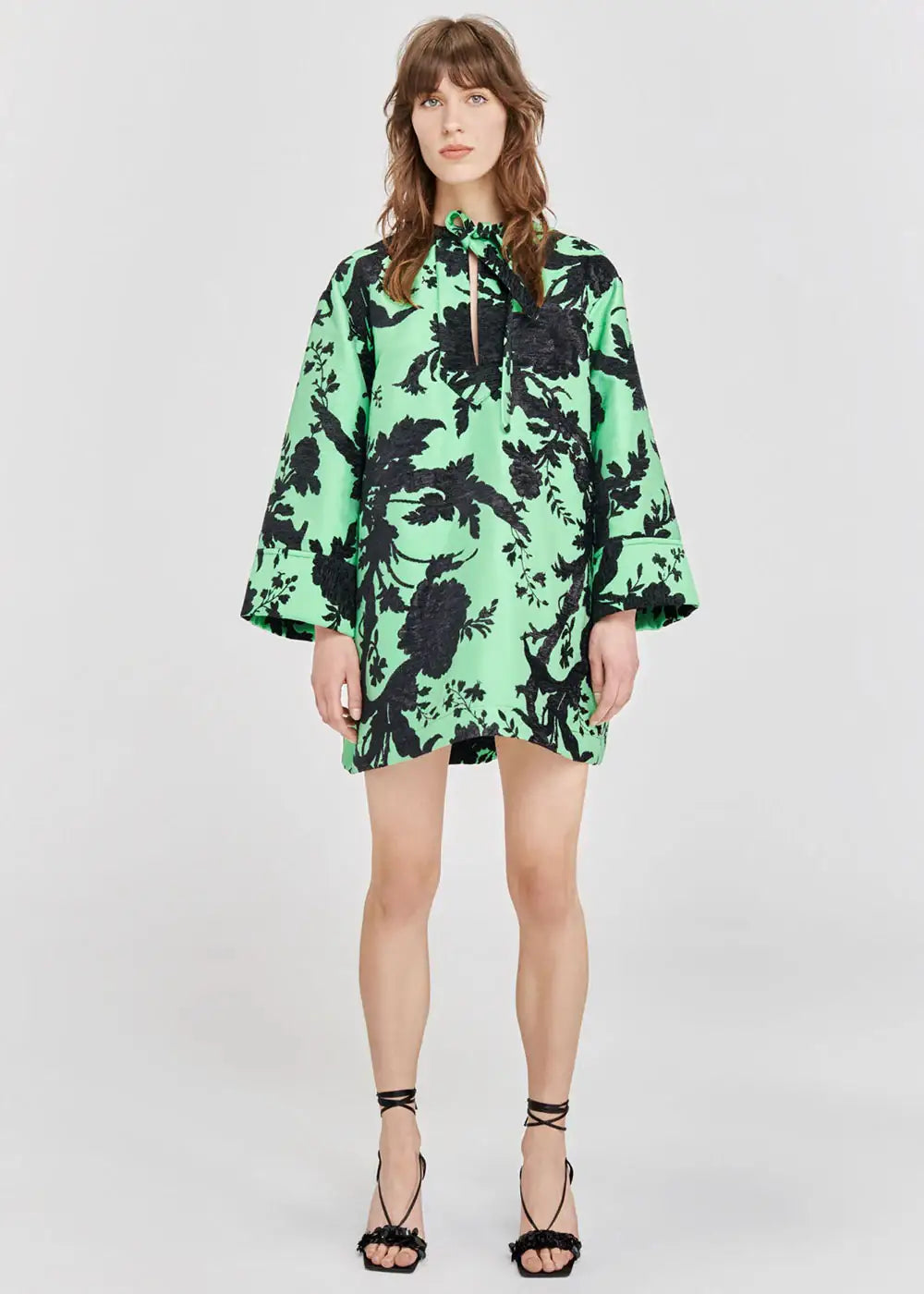 Woman wearing a green mini dress with bold black floral print and flared sleeves