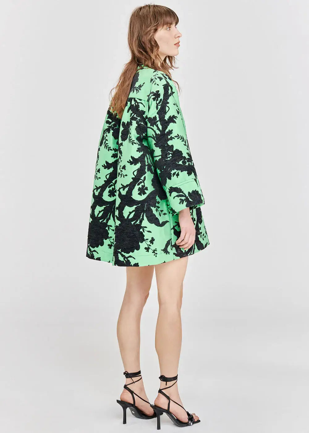 Woman in mint green coat with bold black floral pattern, side view, fashion outfit