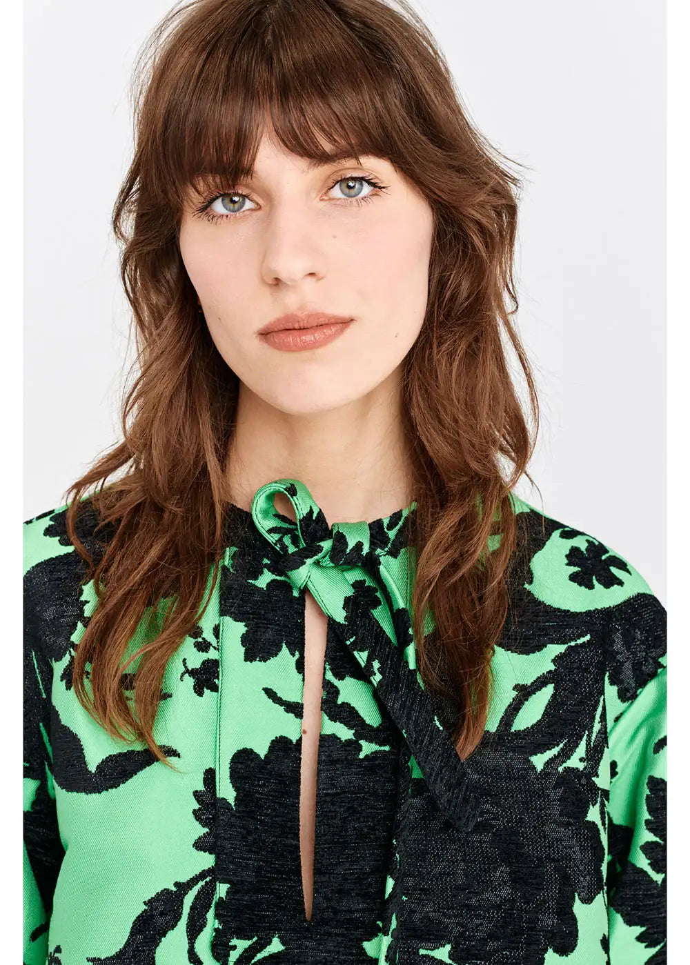 Woman wearing green and black floral blouse with front keyhole tie detail