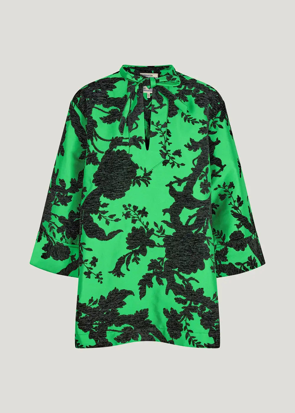 Green tunic top with bold black floral pattern and tie neckline, loose fit sleeves