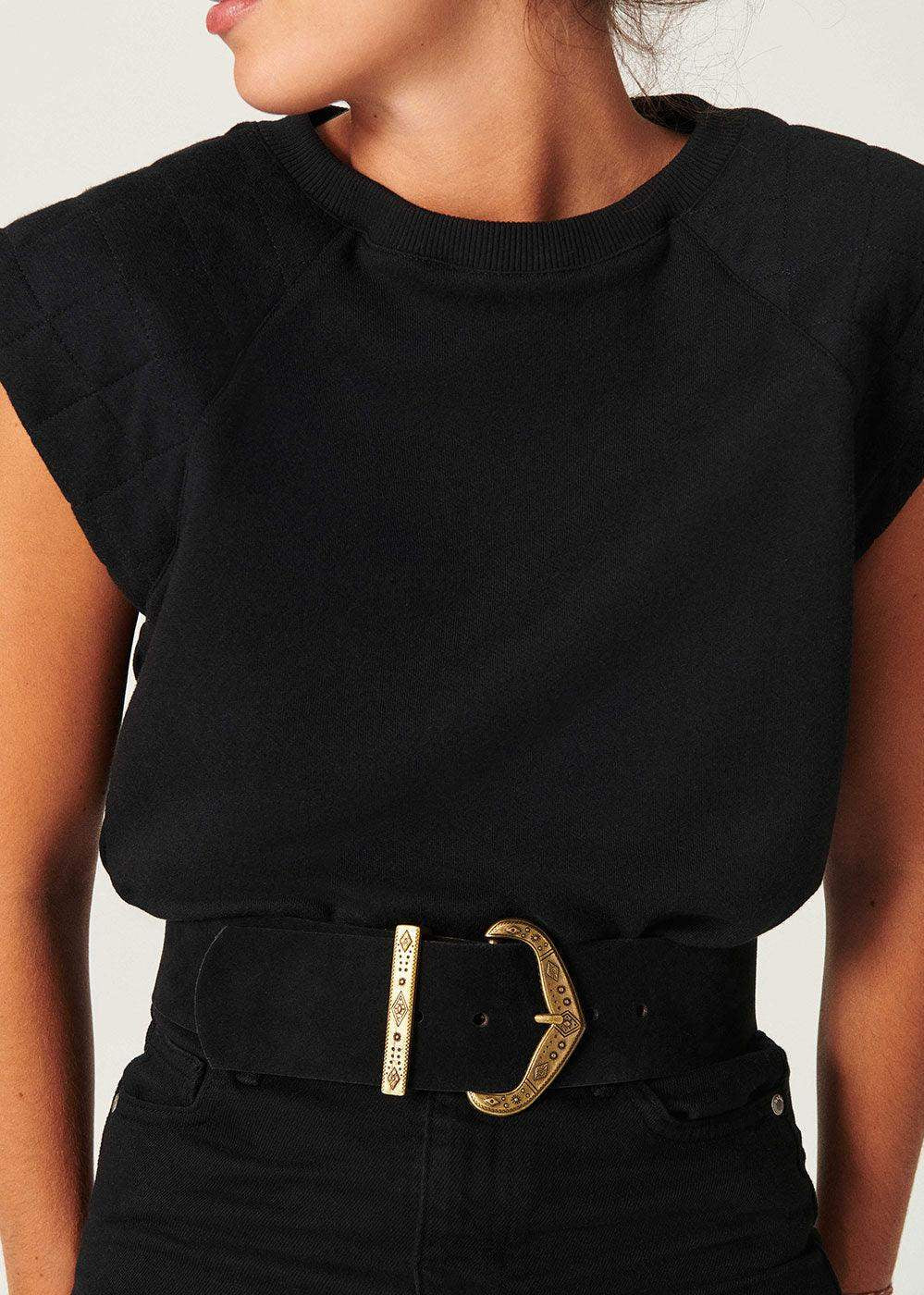 Woman wearing a black suede wide belt with gold engraved buckle over black top and jeans