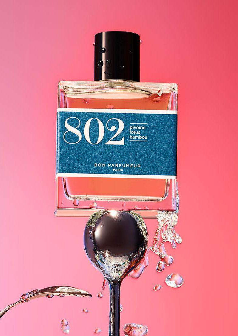 Perfume bottle labeled 802 with water splashes, pink background, modern, fresh fragrance