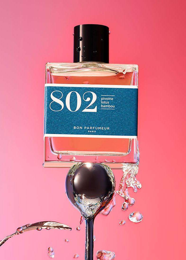 Perfume bottle labeled 802 with water splashes, pink background, modern, fresh fragrance