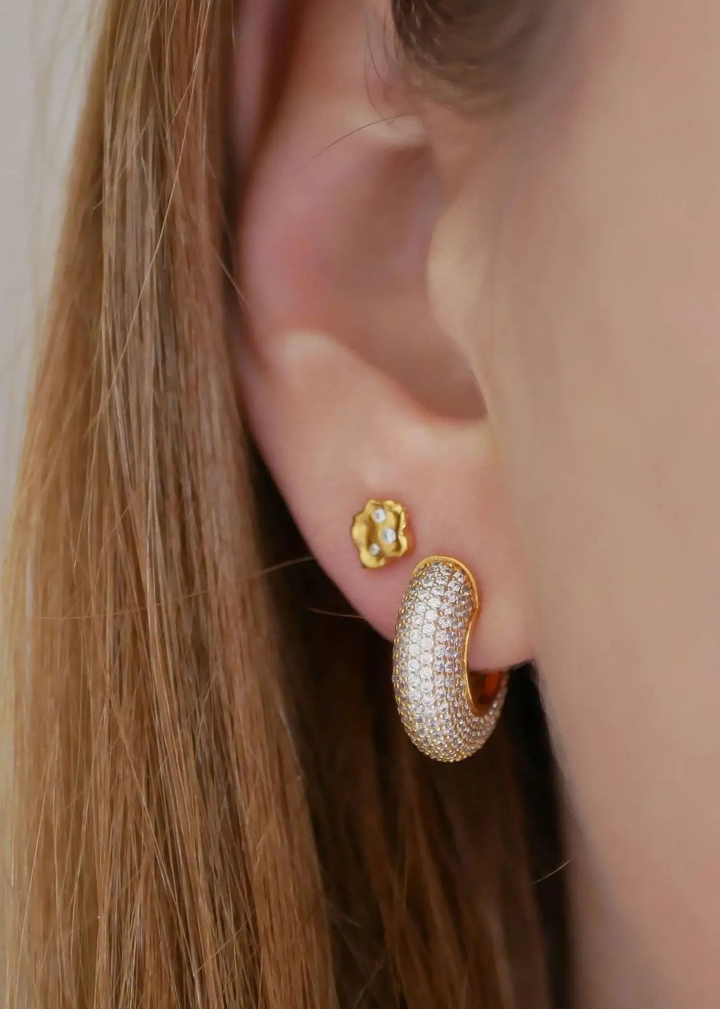 Gold hoop earrings with clear sparkling stones on ear, paired with small gold stud
