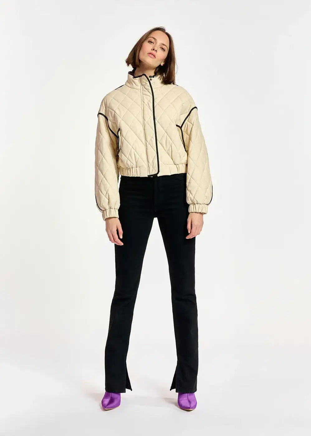Woman wearing black split hem jeans, cream quilted jacket, and purple boots on white background.
