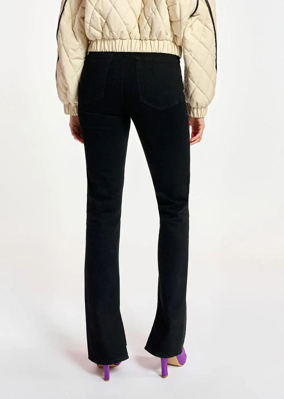 Back view of woman wearing black straight-leg jeans and cream quilted jacket with purple heels