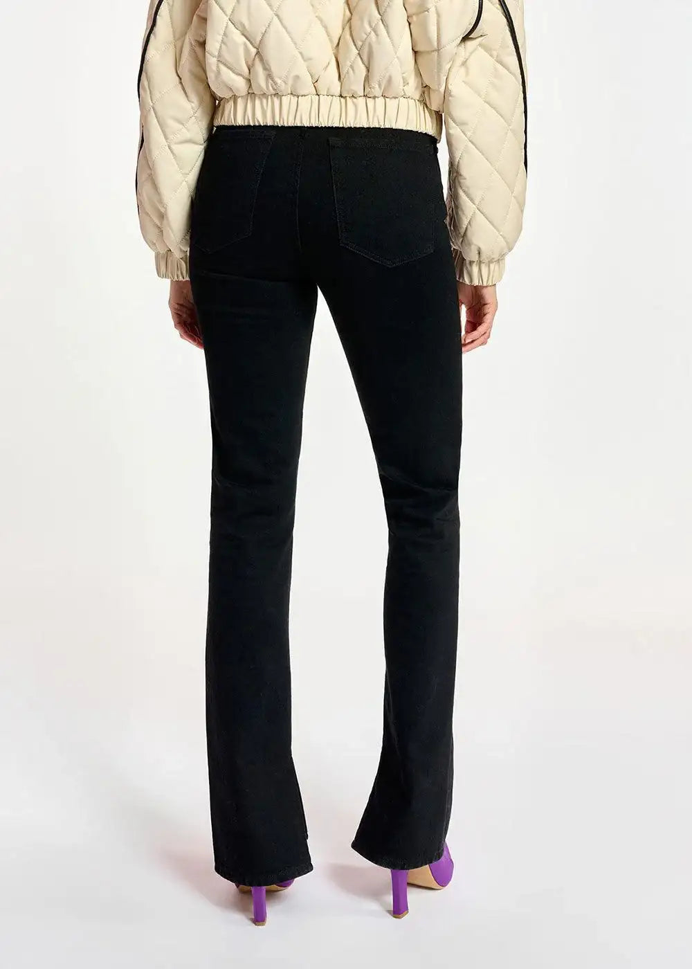 Back view of woman wearing black straight-leg jeans and cream quilted jacket with purple heels