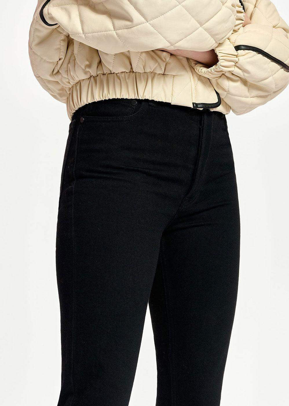 Close-up of high-waisted black jeans paired with a beige quilted jacket