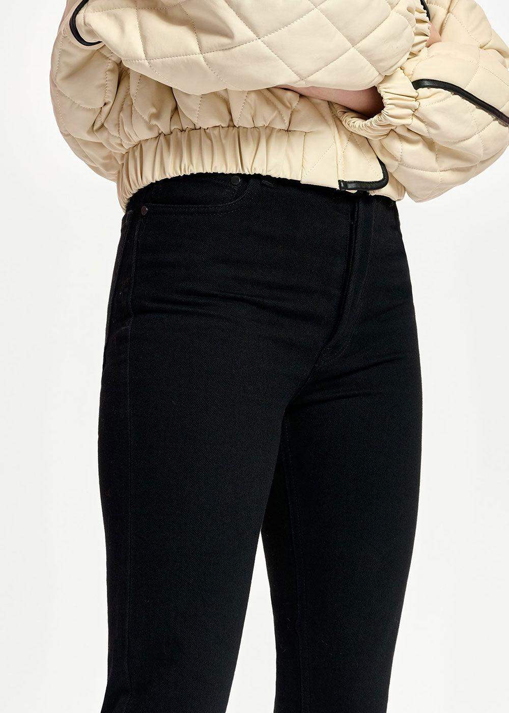 Close-up of high-waisted black jeans paired with a beige quilted jacket