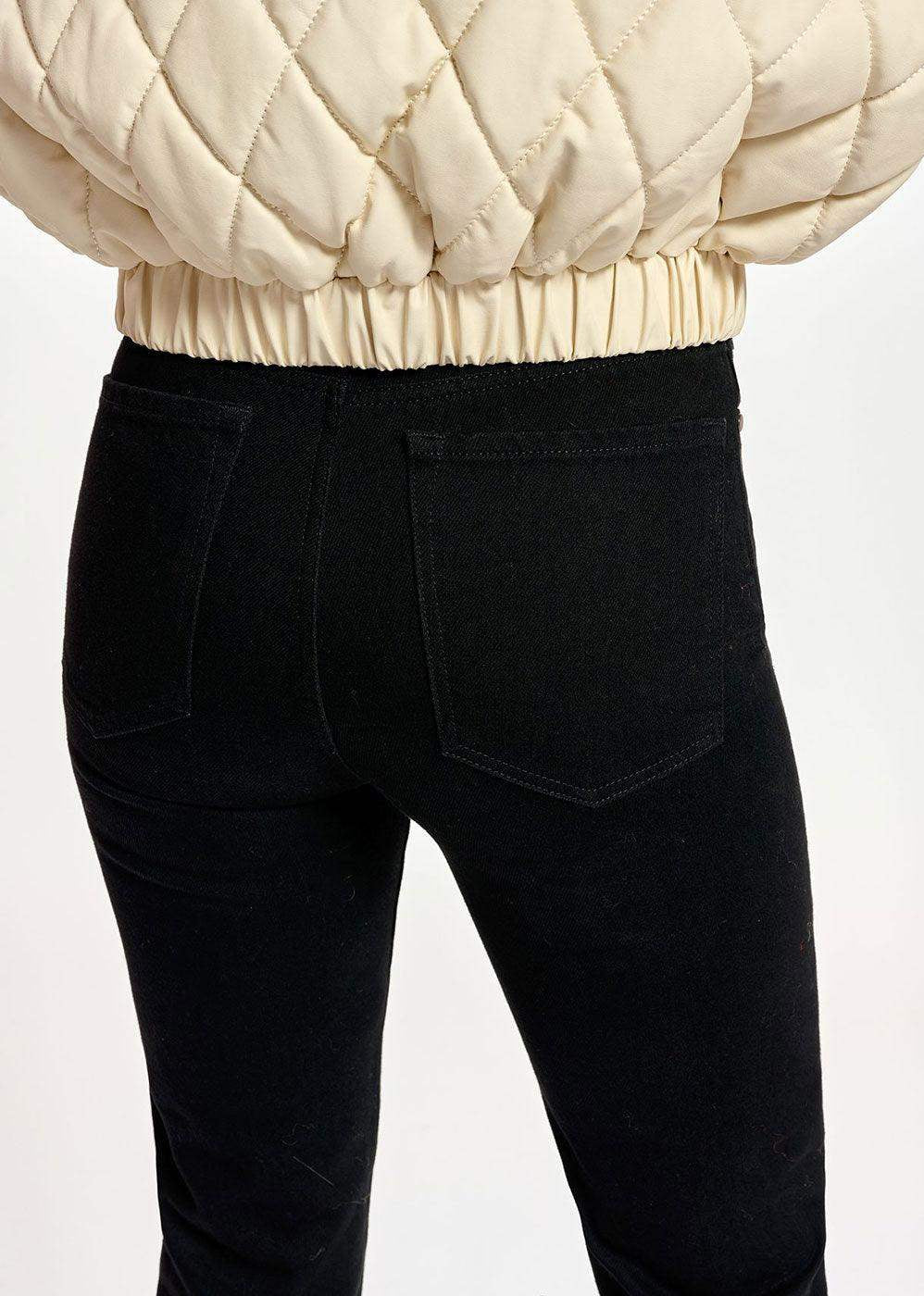 Back view of black high-waisted jeans with rear pockets on a model wearing a cream quilted jacket