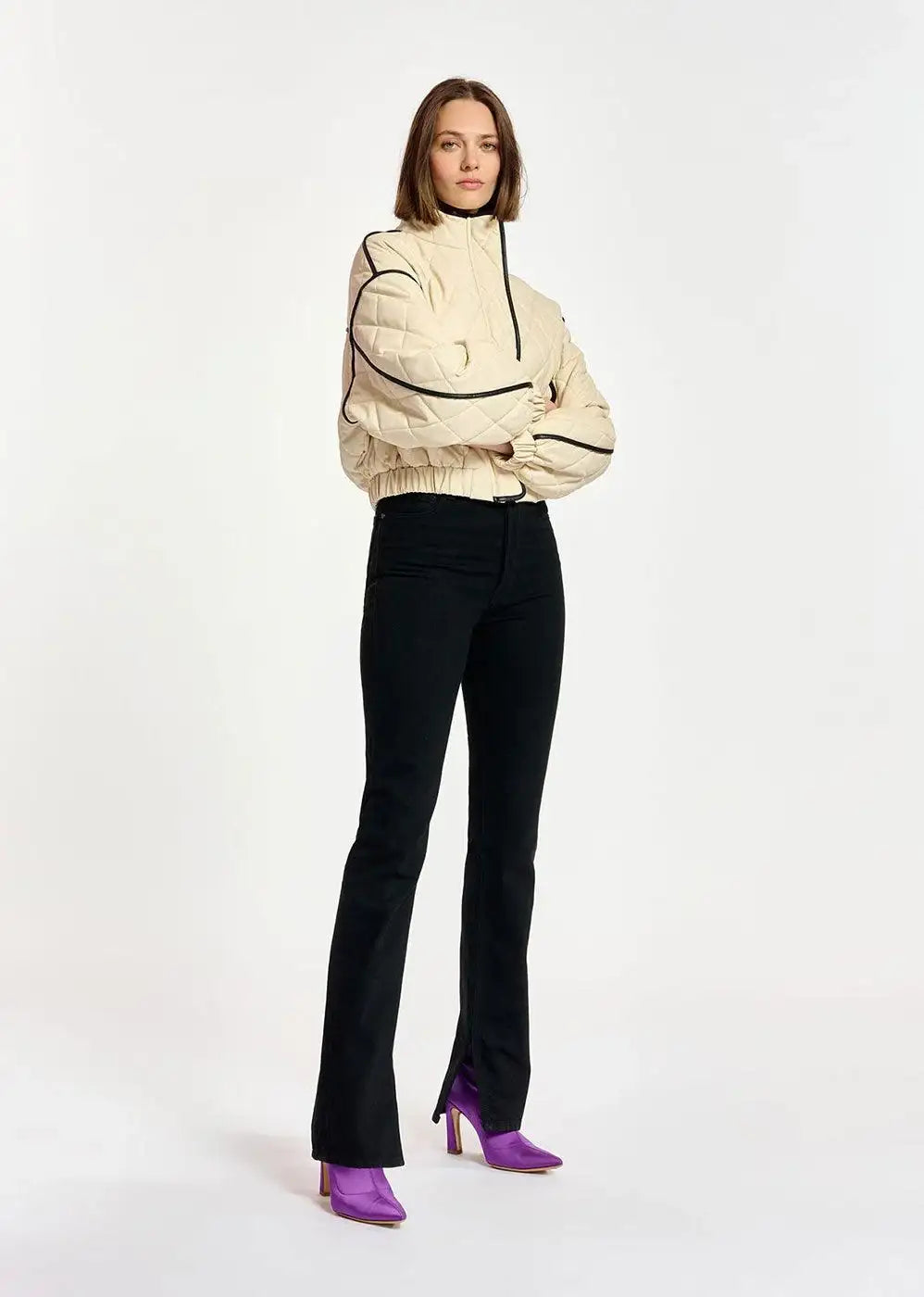 Woman wearing black slim-fit jeans, cream quilted jacket, and purple heels