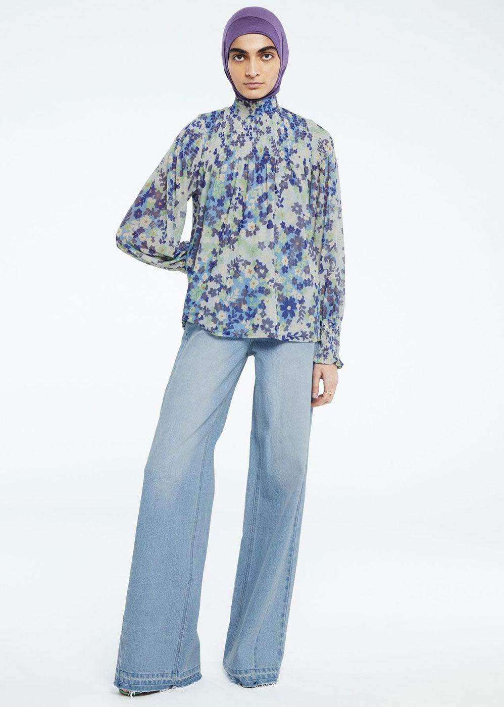 Woman in floral long sleeve blouse, wide-leg light blue jeans, and purple headscarf