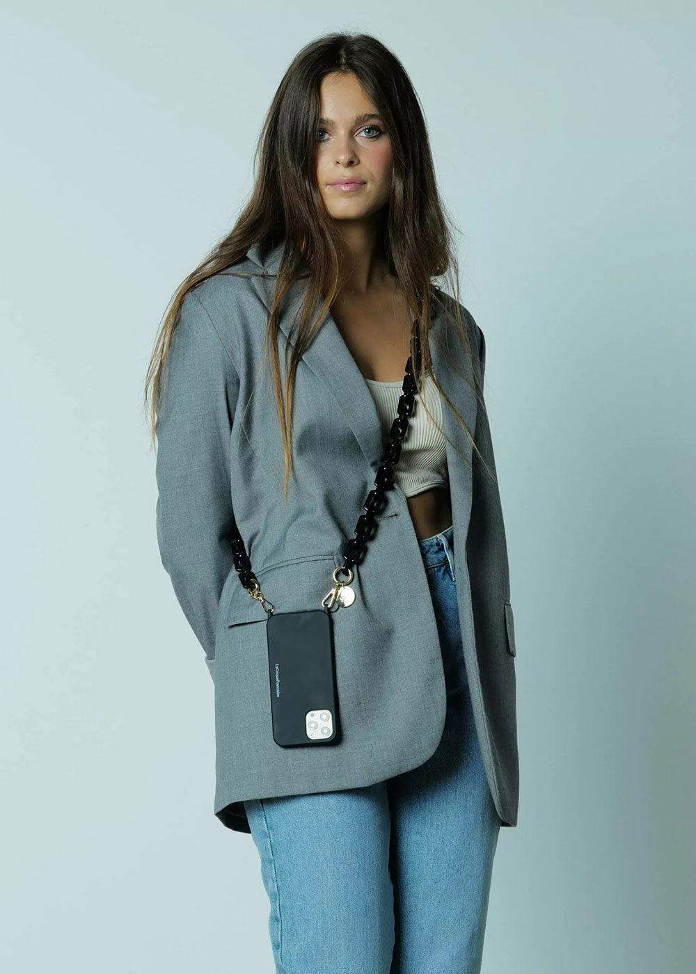 Woman wearing a black phone chain crossbody, grey blazer, white top, and jeans