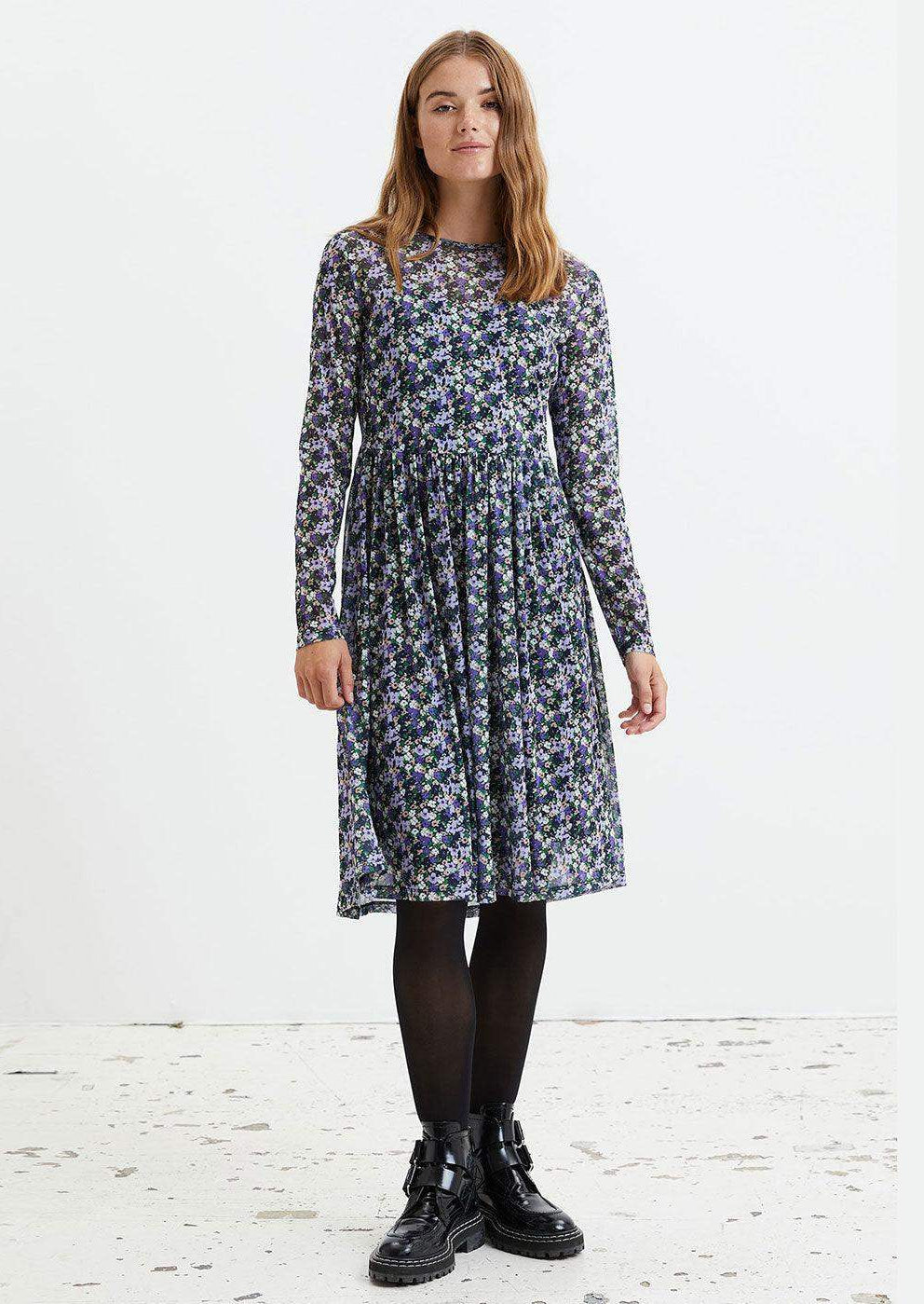 Woman wearing a long sleeve midi dress with blue and purple floral print, black tights, and boots