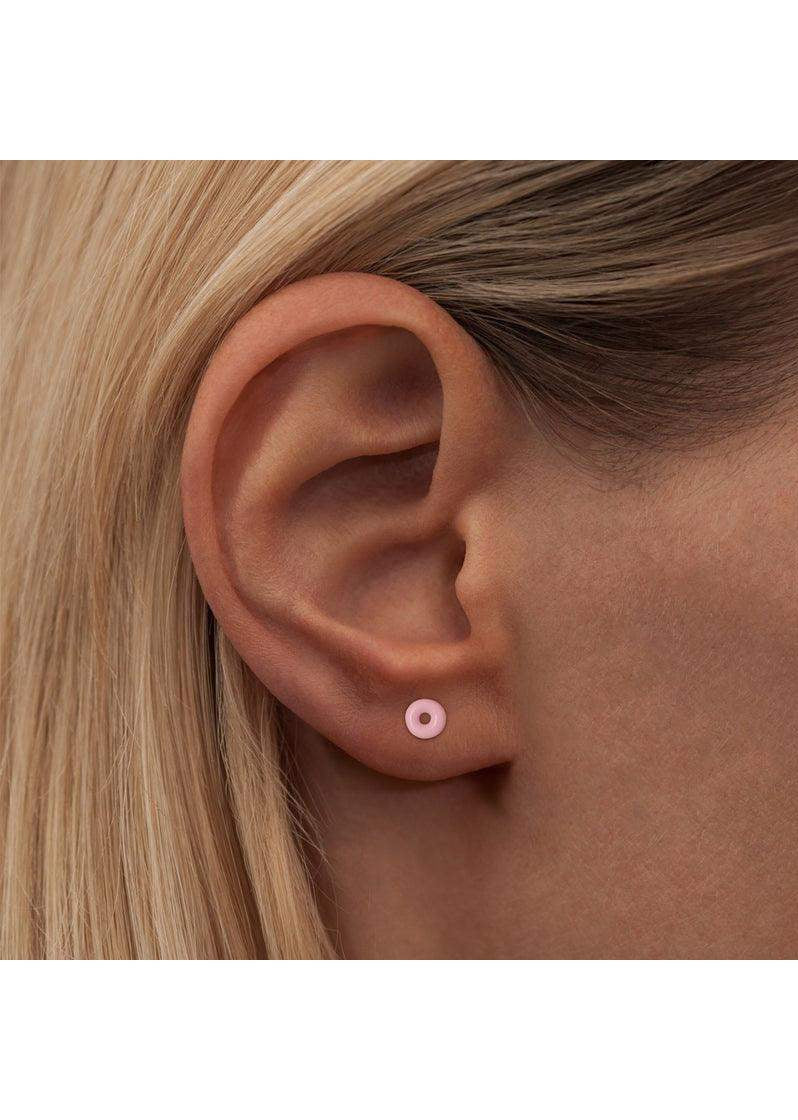 Light pink donut-shaped enamel stud earring worn on earlobe, minimalist jewelry style