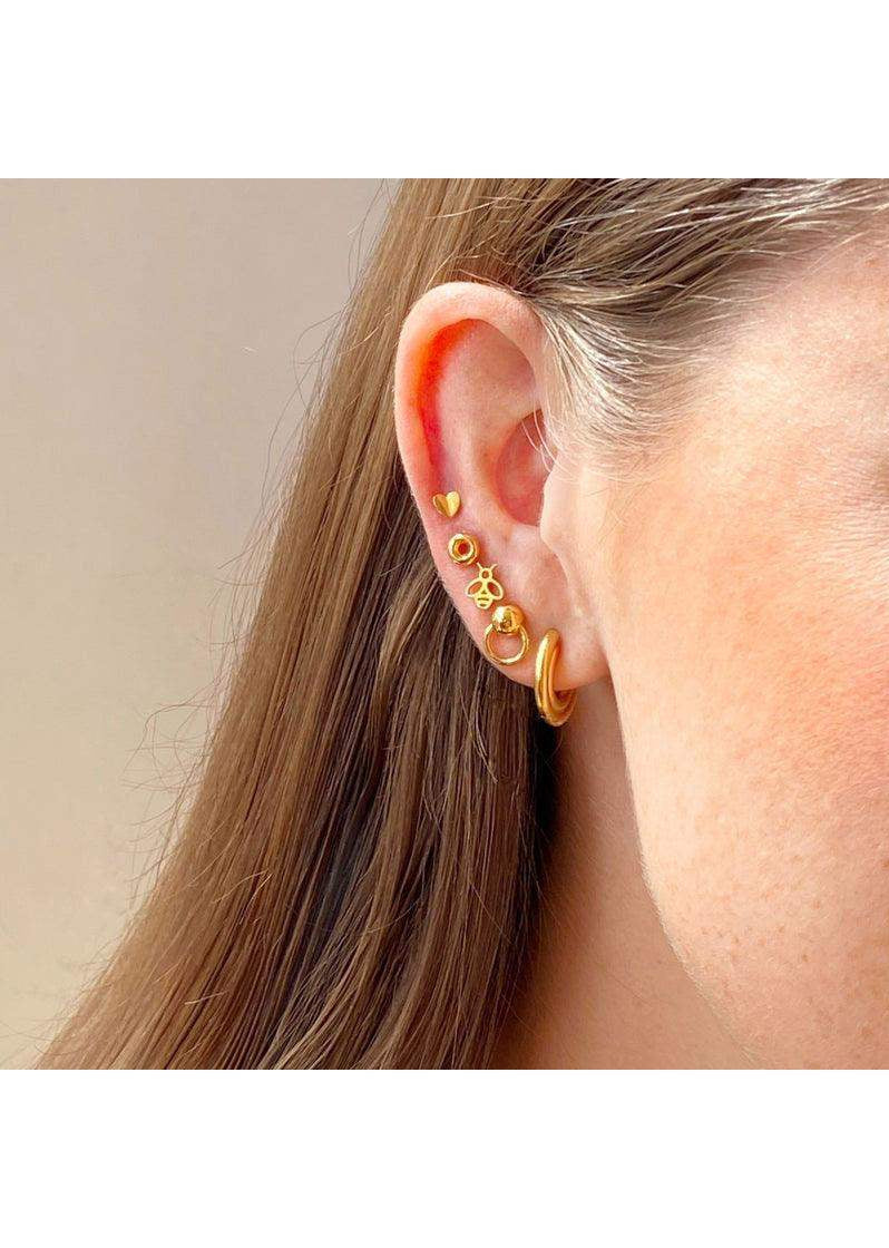 Multiple gold and pink enamel stud earrings arranged on a woman's ear