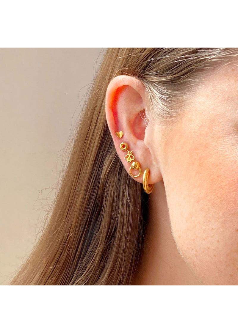 Multiple gold and pink enamel stud earrings arranged on a woman's ear