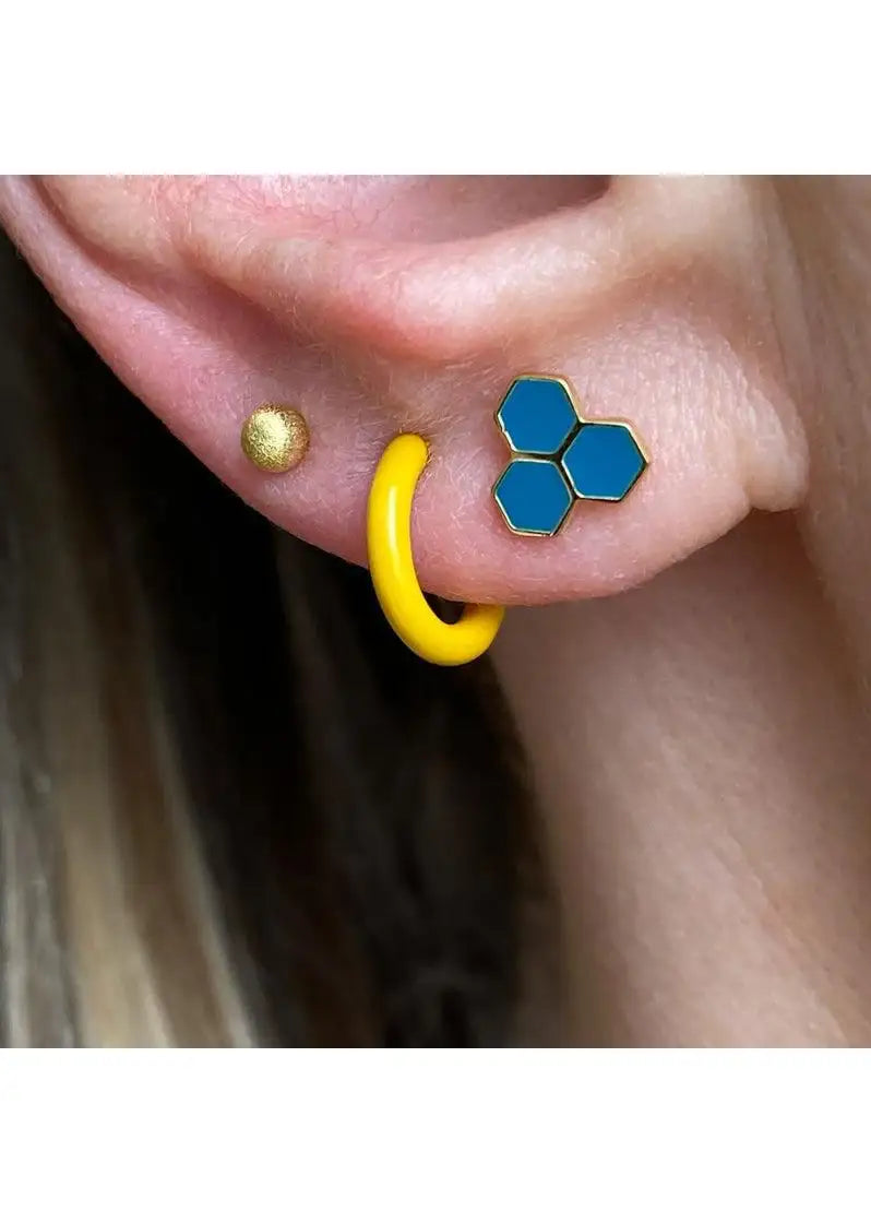 Close-up of ear with blue hexagon stud, yellow hoop, and gold stud earrings