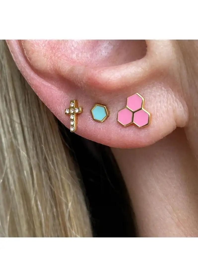 Ear with three gold stud earrings, including a pink hexagon trio, mint hexagon, and cross design